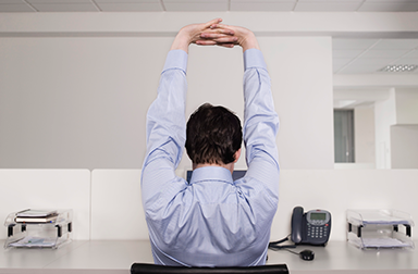 Man sitting at workstation, stretching with fingers interlaced